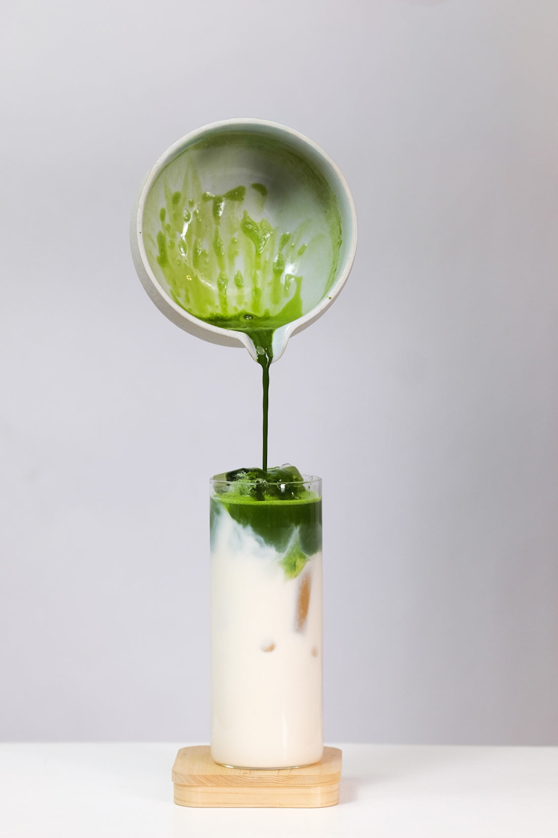 Matcha being poured from a small bowl into a glass with a white background